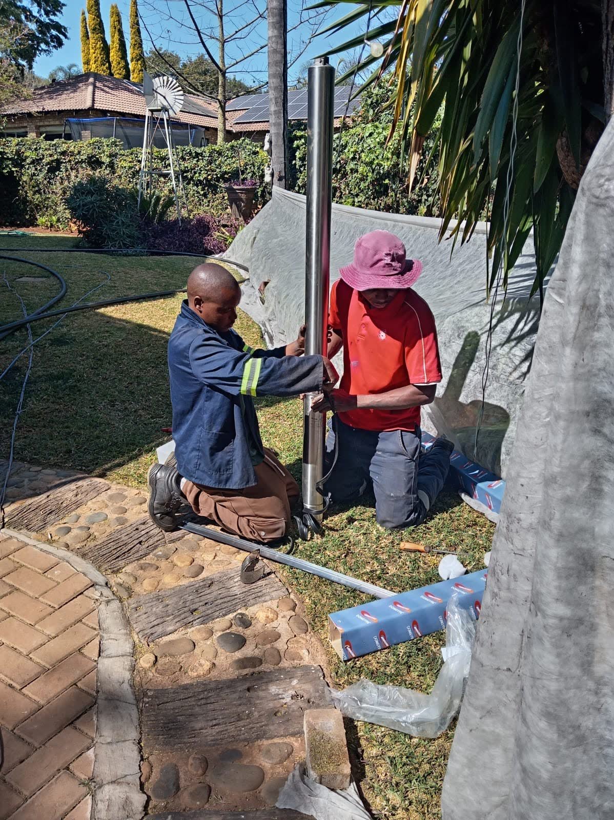 Two technicians installing a submersible borehole pump in a residential garden