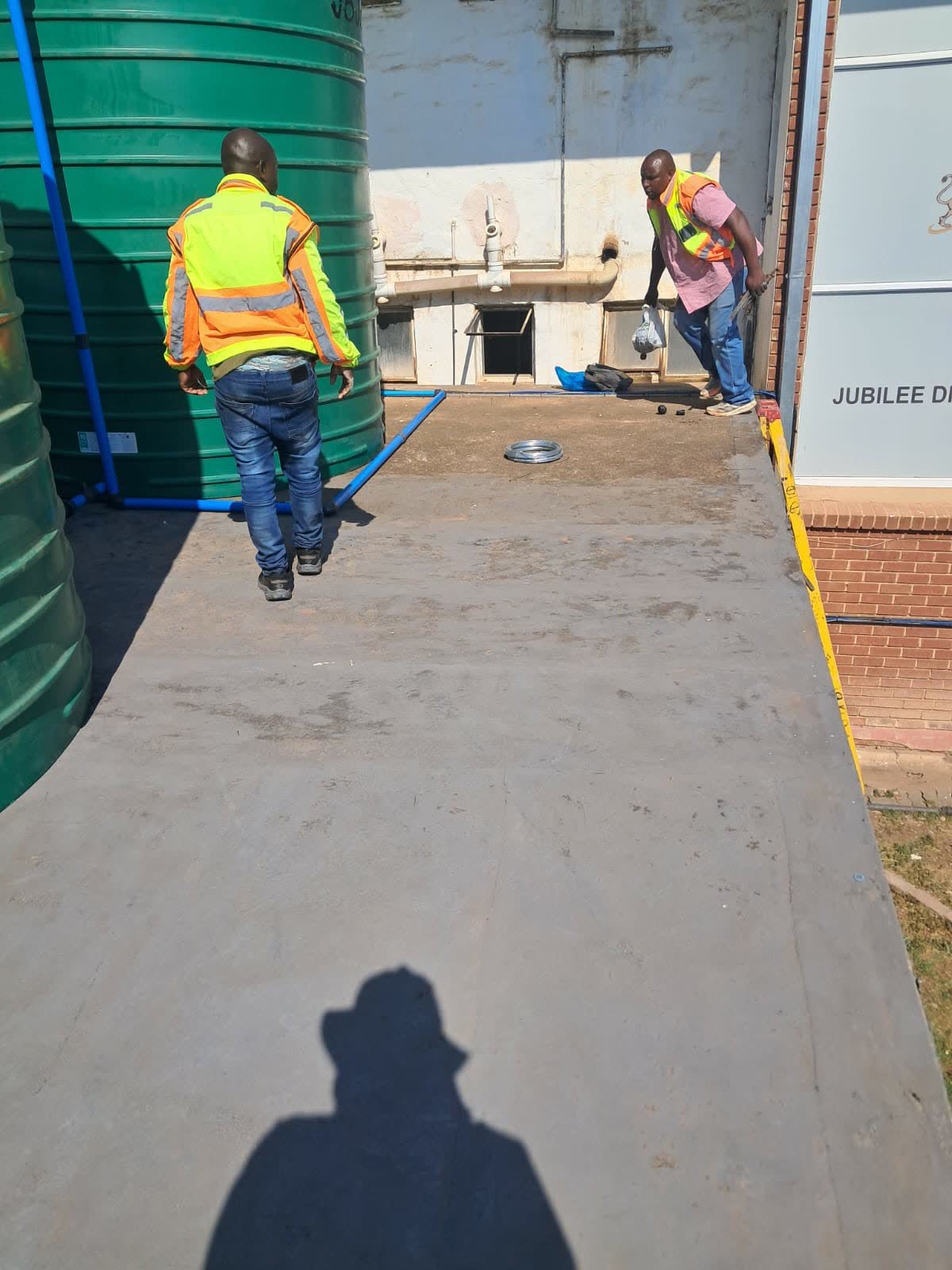 Green JoJo water storage tanks connected with blue piping at a commercial site